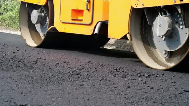 Primer plano, obras de construcción de carreteras con máquina compactadora de rodillos y terminador de asfalto. Rodillo de carretera que pone pavimento de asfalto fresco en la parte superior de la base de grava durante la construcción de carreteras — Vídeo de stock