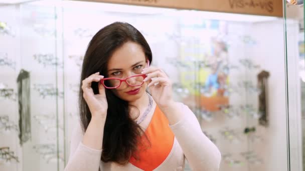 Sexy bela mulher olhando para a câmera. Retrato de cliente feminina sorridente vestindo óculos em loja óptica, em um centro óptico  . — Vídeo de Stock