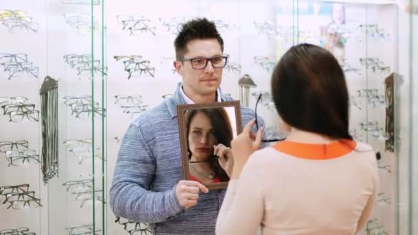 Sexig vacker kvinna kontrollera hennes nya glasögon i en spegel på i optiska store, optik, optiker butik, Glasögon butik, stilig unga manliga säljare håller en spegel — Stockvideo
