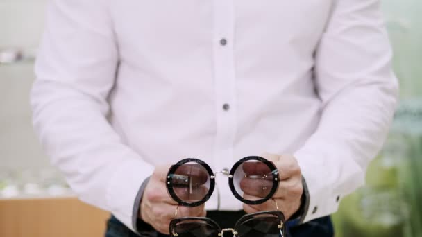 Närbild, mens händer hålla en massa solglasögon, massor av färgglada glasögon samtidigt. mannen är klädd i en vit skjorta — Stockvideo