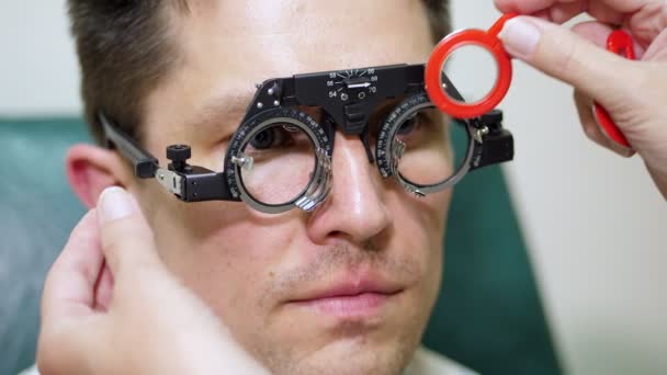 顔クローズ アップ、眼科の検眼医トライアル フレーム、視覚検査装置で患者の男を調べるします。眼科クリニックのビジョンをチェックする男性患者, — ストック動画