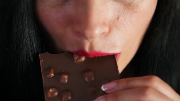 Douce tentation. Gros plan recadré d'une femelle à lèvres rouges mordant sur un chocolat, lèvres d'une belle femme brune sexy mangeant du chocolat aux noisettes — Video