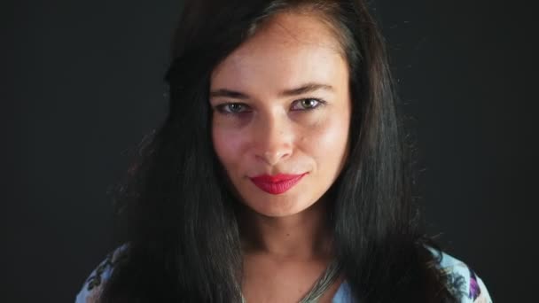 Portrait of a sexy brunette woman with red lips who eroticly and playfully eats black chocolate with hazelnuts and looking at camera in studio. dark gray background. — Stock Video