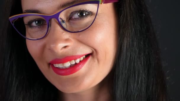 Retrato de una mujer morena sexy con labios rojos que erótica y juguetonamente se prueba gafas con estilo, gafas y mirando sexualmente a la cámara en el estudio. fondo gris oscuro . — Vídeo de stock