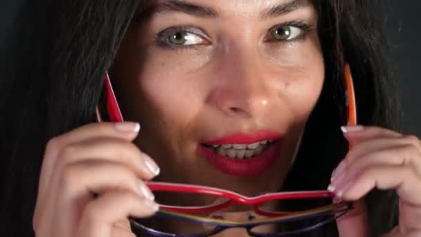 Porträt einer sexy brünetten Frau mit roten Lippen, die erotisch und spielerisch verschiedene stylische Brillen, Brillen und Blicke in die Kamera im Studio anprobiert. — Stockvideo