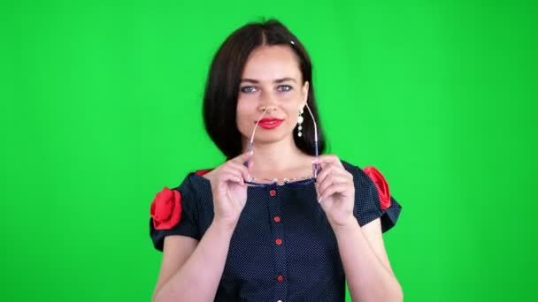 Grön bakgrund, chromeakey. Porträtt av en sexig brunett kvinna med röda läppar, i eleganta Glasögon, Glasögon, flyttar eroticly, lekfullt, tittar sexuellt på kameran, poserar i studio. — Stockvideo