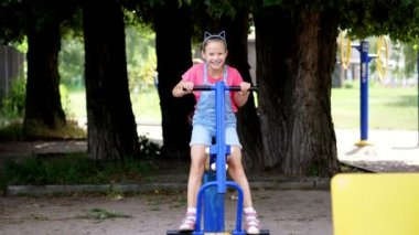 gülümseyen, mutlu sekiz yaşındaki kız, park, yaz, tatil sırasında sıcak gün açık egzersiz donanımları, açık havada, egzersizleri yaparken meşgul.