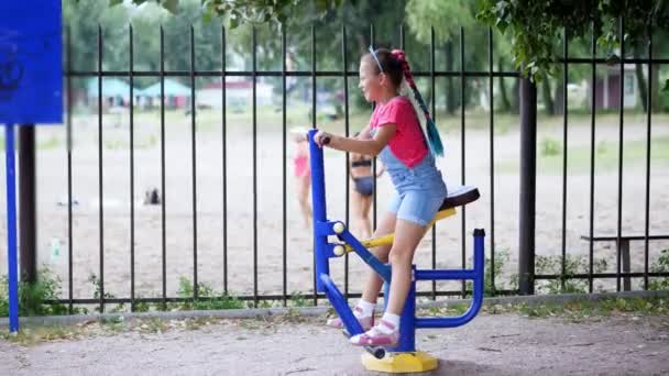 Sorridente, felice ragazza di otto anni impegnata, facendo esercizi su attrezzature per esercizi all'aperto, all'aperto, nel parco, estate, giornata calda durante le vacanze . — Video Stock