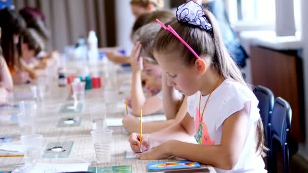 Lezione di disegno, in classe, i bambini disegnano con i colori, padroneggiare la tecnica di disegno su vetro. in primo piano una bella bionda di otto anni con una passione disegna — Video Stock