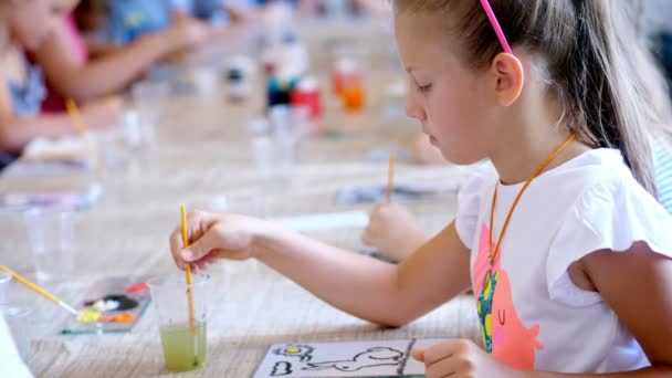 Salle de classe de dessin, belle fille blonde de huit ans avec une passion dessine avec des couleurs, maîtriser la technique de dessin sur verre. Laver au pinceau pour dessiner — Video