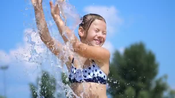 Usměvavý osm let stará dívka v plavkách se baví v postřiku v ulici městské kašny, venku, park, letní, horký slunečný den během dovolené. — Stock video