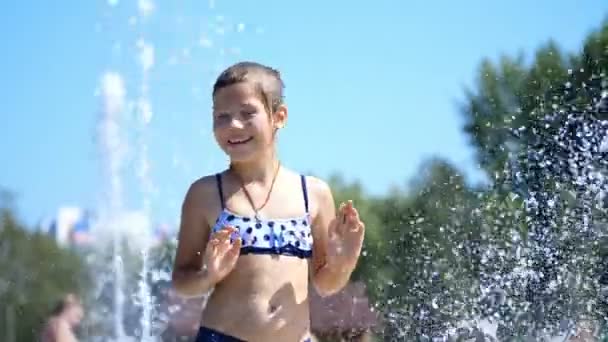 Sonriente, feliz niña de ocho años en traje de baño divertirse en salpicaduras en la fuente de la ciudad de la calle, al aire libre, en el parque, verano, día soleado caliente durante las vacaciones . — Vídeos de Stock