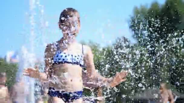 Smiling, happy eight year old girl in swimsuit having fun in splashes in street city fountain, outdoors, in park, summer, hot sunny day during vacation. — Stock Video