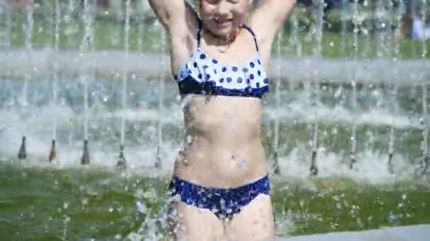 Sonriente, feliz niña de ocho años en traje de baño divertirse en salpicaduras en la fuente de la ciudad de la calle, al aire libre, en el parque, verano, día soleado caliente durante las vacaciones . — Vídeos de Stock