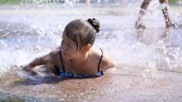 Sorridente, felice bambina di otto anni in costume da bagno divertirsi in spruzzi in fontana di città di strada, all'aperto, nel parco, estate, calda giornata di sole durante le vacanze . — Video Stock