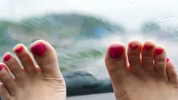 Primer plano de las piernas femeninas con barniz de uñas brillante, pedicura. yace frente al parabrisas. está lloviendo, limpiaparabrisas del coche están trabajando . — Vídeo de stock