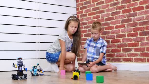 Garçon et fille de sept ans jouent robots électroniques, voitures, jouets modernes sur la radio-commande. nouvelles technologies dans l'industrie du jeu pour enfants. petits génies — Video