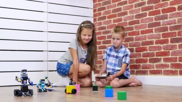 Niño y niña de siete años juegan robots electrónicos, coches, juguetes modernos en el control de radio. nuevas tecnologías en la industria de los juegos para niños. pequeños genios — Vídeo de stock