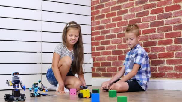 Menino e menina de sete anos de idade jogar robôs eletrônicos, carros, brinquedos modernos no controle de rádio. novas tecnologias na indústria de jogos infantis. pequenos génios — Vídeo de Stock