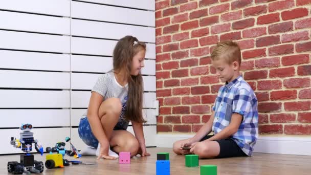 Menino e menina de sete anos de idade jogar robôs eletrônicos, carros, brinquedos modernos no controle de rádio. novas tecnologias na indústria de jogos infantis. pequenos génios — Vídeo de Stock