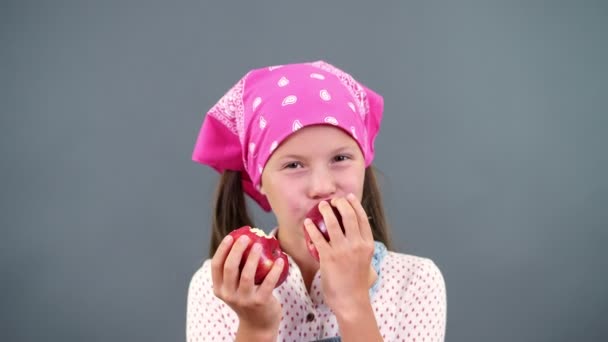 Linda chica campesina sosteniendo en las manos dos grandes manzanas rojas maduras, come, las muerde sobre un fondo gris en el estudio. Concepto de nutrición saludable . — Vídeo de stock