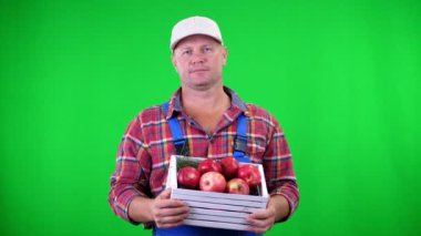 gülümseyen bir ahşap kutu kırmızı olgun organik elma ile tutarak yakışıklı erkek çiftçi portresi. Studio yeşil arka plan üzerinde. Tablonuza sağlıklı gıda