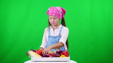 şirin, gülümseyen, küçük çiftçi kız farklı taze sebze, bir kutusunda gösterir hasat. Studio yeşil arka plan üzerinde. Tablonuza sağlıklı beslenme sağlıklı gıda.