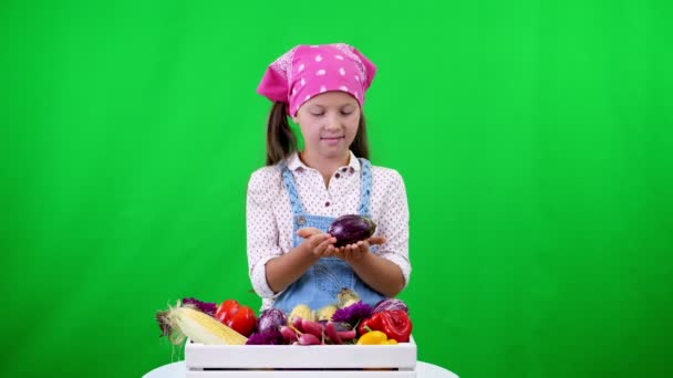 Roztomilé, usměvavé, malý farmář dívka ukazuje pole s různými čerstvou zeleninou, sklizeň. na zeleném pozadí ve studiu. Zdravé potraviny na váš stůl, zdravá výživa. — Stock video