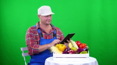 Chromakey, yeşil renkli ve kutusu farklı sebze, dolu bir tablete studio tutarak yakın çekim, yakışıklı erkek çiftçi ekose gömlek ve mavi tulum. sayma, ürün hasat sebze