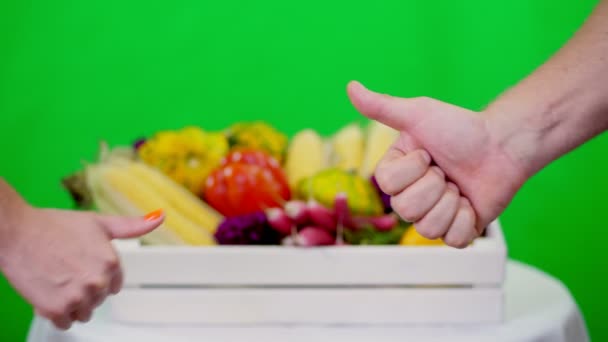 Close-up, Duas mãos mostrando polegares para cima sinal, Ok sinal, contra Chromakey, fundo verde e uma caixa cheia de vegetais diferentes, em estúdio. conceito de contagem de culturas, colheita de legumes — Vídeo de Stock