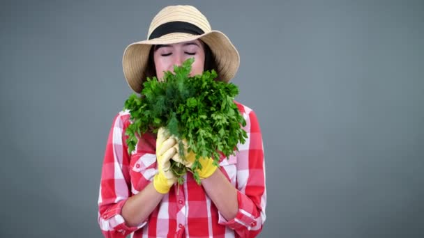 格子縞のシャツ、手袋、帽子の持株の笑みを浮かべて女性農民の肖像画に新鮮な緑の束がにおいがするスタジオで、灰色の背景に、パセリ、緑します。あなたのテーブルに健康食品 — ストック動画