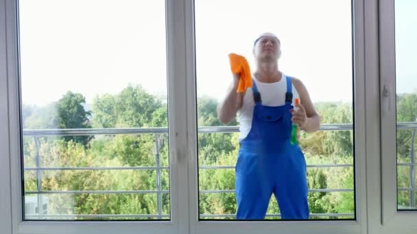 Vista a través de la ventana, atractivo trabajador de servicio de limpieza masculino, en mono azul y en blaser, Ventana de limpieza por pulverización de productos de limpieza, utilizando detergente, trapo — Vídeo de stock