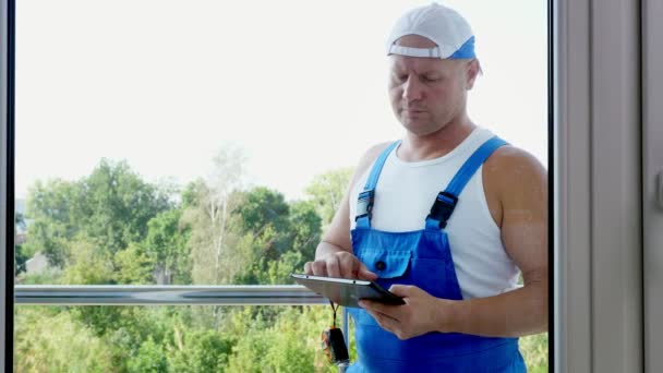 Der attraktive Bauarbeiter macht sich Notizen in Tablets. Servicekräfte installieren Fenster — Stockvideo