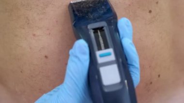 Yakın çekim, güzellik uzmanı kadın eller eldiven saç kesimi vücut çıplak kıllı insan saçı, göğsüne, içinde gövde, bir kesme makinesi, elektrikli ustura, trimer ile tüm vücut. Beyaz arka plan üzerinde.