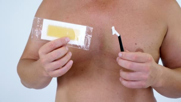 Close-up, Mens handen houd strepen met wax en een scheermes, verschillende betekent voor epileren, Safety razor en wax strips voor epileren op mannelijke naakte borst achtergrond. — Stockvideo