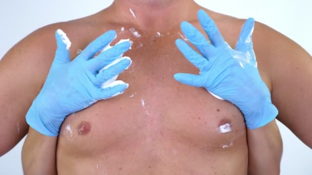 Primer plano, las manos cosmetólogas femeninas con guantes extendieron espuma de afeitar blanca sobre el torso masculino peludo desnudo, el pecho sexualmente. sobre fondo blanco . — Vídeo de stock