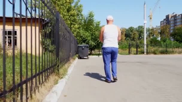 Vista trasera, el hombre lleva un paquete de basura en sus manos, saca basura. día caluroso de verano. ecología. separación de residuos, limpieza del medio ambiente — Vídeos de Stock