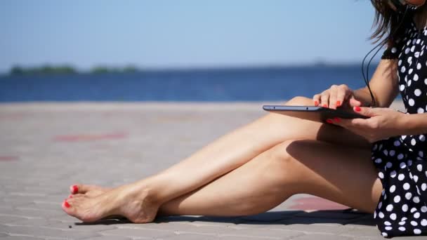 detail, dívka pracuje na tabletu, ženské ruce, nohy s jasně červená manikúra, nehty, pedikúra, na pláži, na horkém letním dni, v blízkosti moře