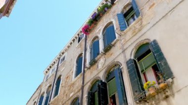 Venice, İtalya - 7 Temmuz 2018: güzel eski mimari Venedik, eski yeşil Panjur ve mavi gökyüzü, sıcak yaz gününde karşı denizlik üzerinde çiçekler olan bir ev,
