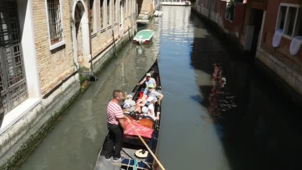 VENICE, ITALY - JULY 7, 2018: narrow canal between the ancient houses of Venzia, hot summer day. traditional Venetian gondola floats along the canal, carries tourists — Stock Video