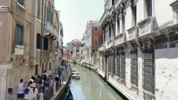 VENICE, ITALY - JULY 7, 2018: narrow canal between the ancient houses of Venzia, hot summer day. tourists walk along the ancient streets along the canals — Stock Video