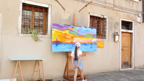ショート パンツとキャップで女児が夏の暑い日に、ベニスの通りに明るい絵を調べヴェネツィア, イタリア - 2018 年 7 月 7 日。. — ストック動画