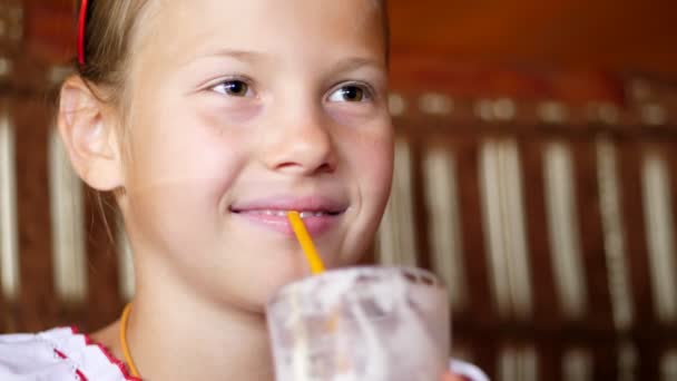 Счастливая улыбающаяся девочка-подросток пьет молочный коктейль в кафе. она одета в украинскую национальную одежду, вышивку, вишиванку — стоковое видео