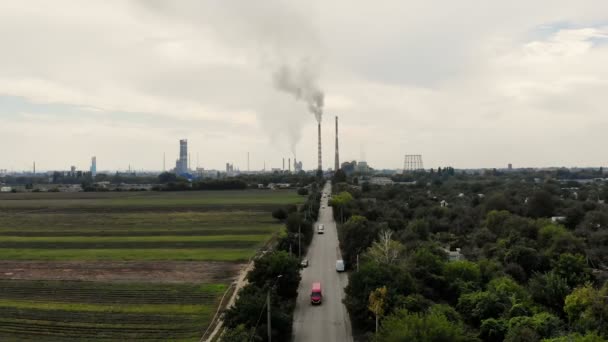 Aero. no meio do campo, uma estrada com carros que leva a uma grande planta, dois altos, grandes, chaminés fumantes. O fumo cinzento sai dos canos. ecologia, poluição do ambiente . — Vídeo de Stock