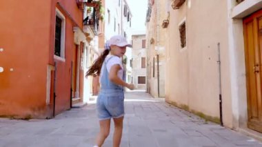 Venice, İtalya - 7 Temmuz 2018: eski evleri, bir genç kız arasında Venedik, dar bir cadde boyunca bir çocuk, şort ve bir blazer çalışır. yaz sıcak gün. Arkadan görünüm.