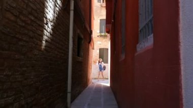 Venice, İtalya - 7 Temmuz 2018: Venedik çok dar bir sokakta sonunda bir şapka ve bir sırt çantası, bir genç kadın turist standları ve bakar, mimari inceliyor.