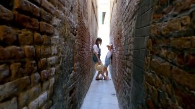 Venice, İtalya - 7 Temmuz 2018: Venedik, çok dar sokak arasında eski evlerin duvarları, bir genç kız, çocuk ve genç kadın, şort ve şapkalar stand. sıcak yaz günü.