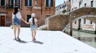 Venice, İtalya - 7 Temmuz 2018: genç bir kadın ve bir çocuk kız aynı denim tulum, şort, Venedik sokaklarında yürümek, küçük bir köprü kanal yükselişi. sıcak yaz günü.