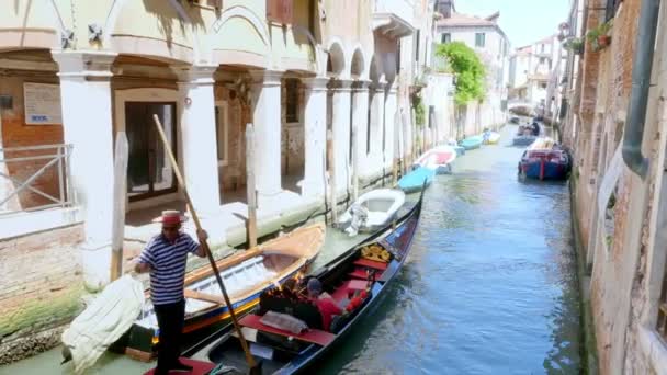 VENECIA, ITALIA - 7 DE JULIO DE 2018: canal estrecho entre las antiguas casas de Venzia, caluroso día de verano. góndola veneciana tradicional navega a lo largo del canal, lleva a los turistas — Vídeo de stock