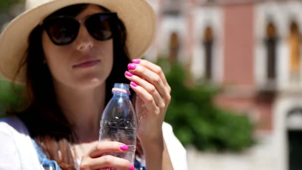 Venice, Olaszország - július 7-én 2018-ban: Egy fiatal nő, napszemüveggel és egy kalap az ivóvíz tiszta, tiszta alpesi egy üveg, háttérben a velencei építészet, a forró nyári napon. — Stock videók
